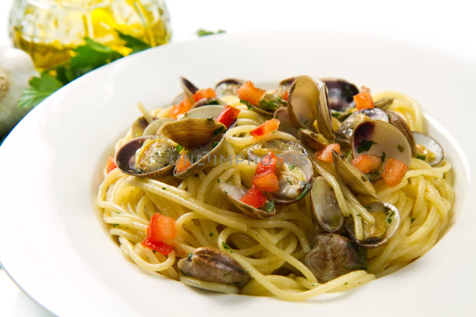 white dish of spaghetti,clams , tomatoes, oil and parsley