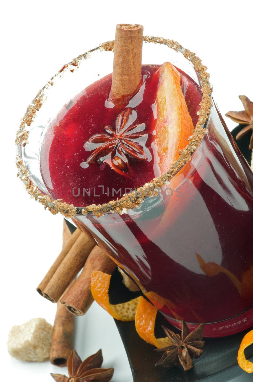 Glass of Mulled Wine and Spices with Cinnamon Stick, Orange, Anise Star and Sugar on Black Saucer closeup on white background