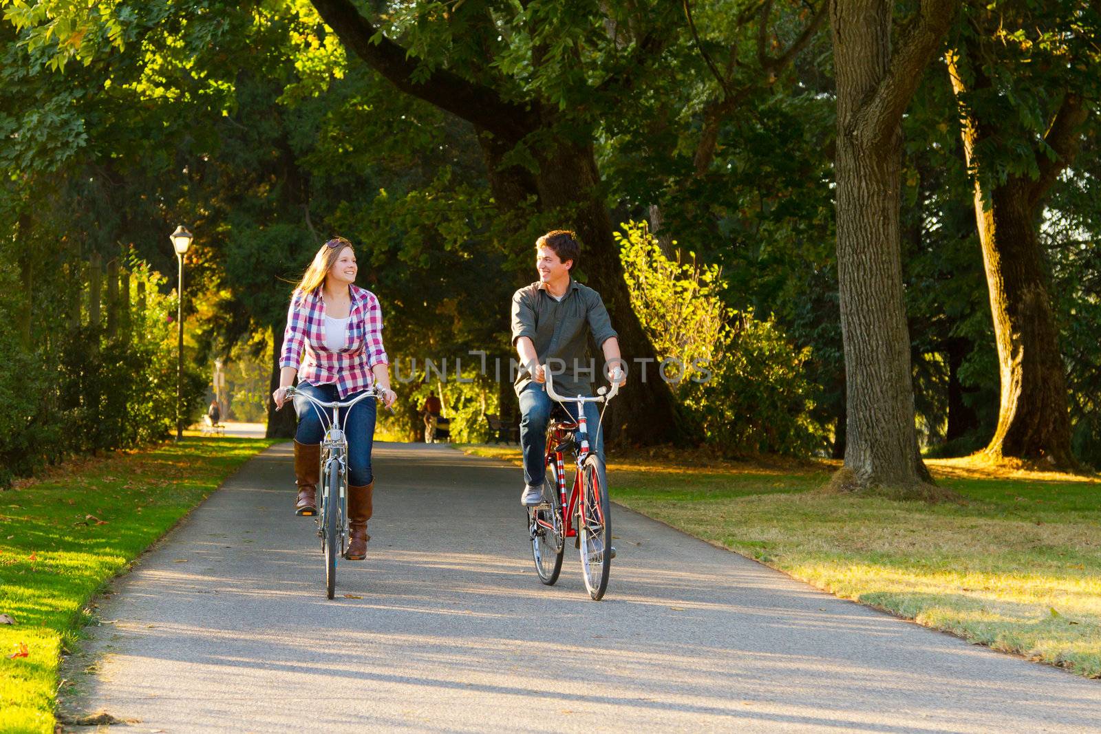 A man and a woman with their bicycles on a bike path in an outdoor park setting.