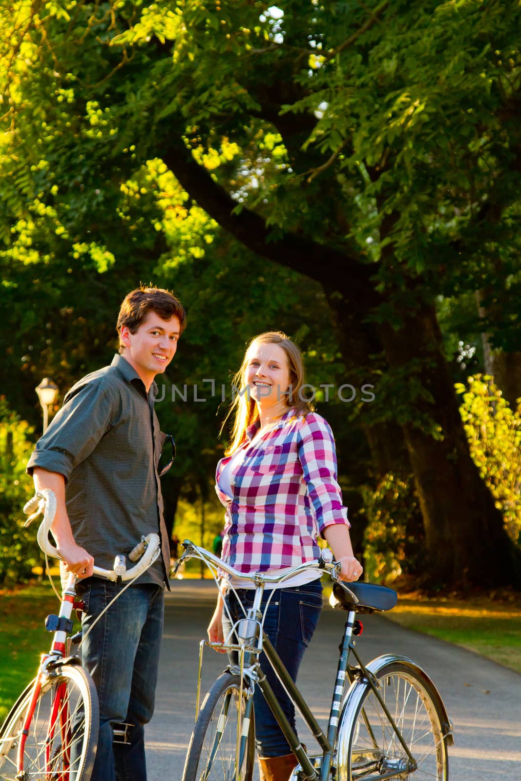 A man and a woman with their bicycles on a bike path in an outdoor park setting.
