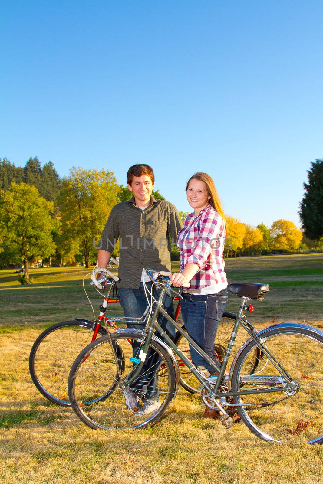 A couple poses for this portrait in a field with their bicycles.