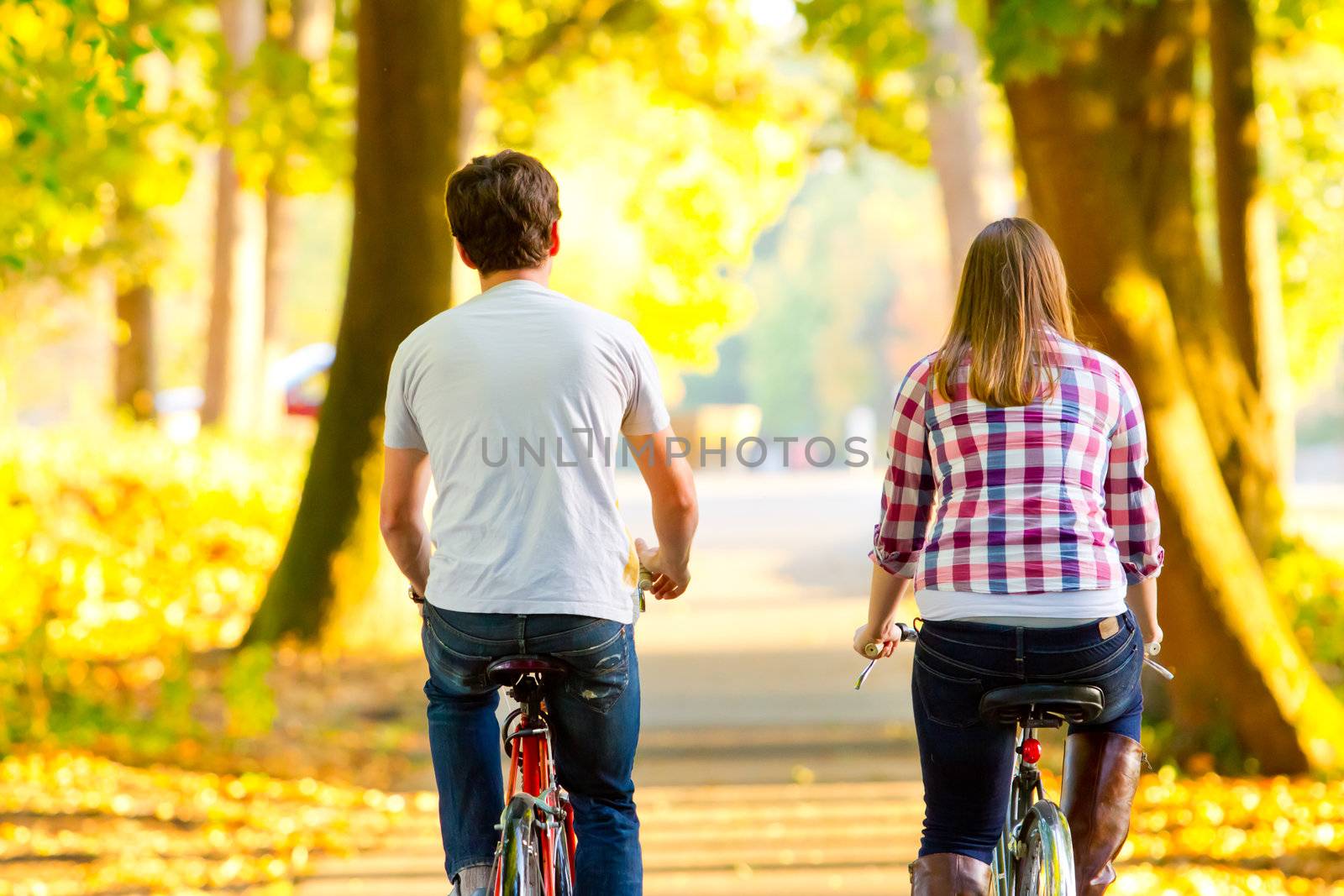 A couple rides their bikes together along a bicycle path in the fall.