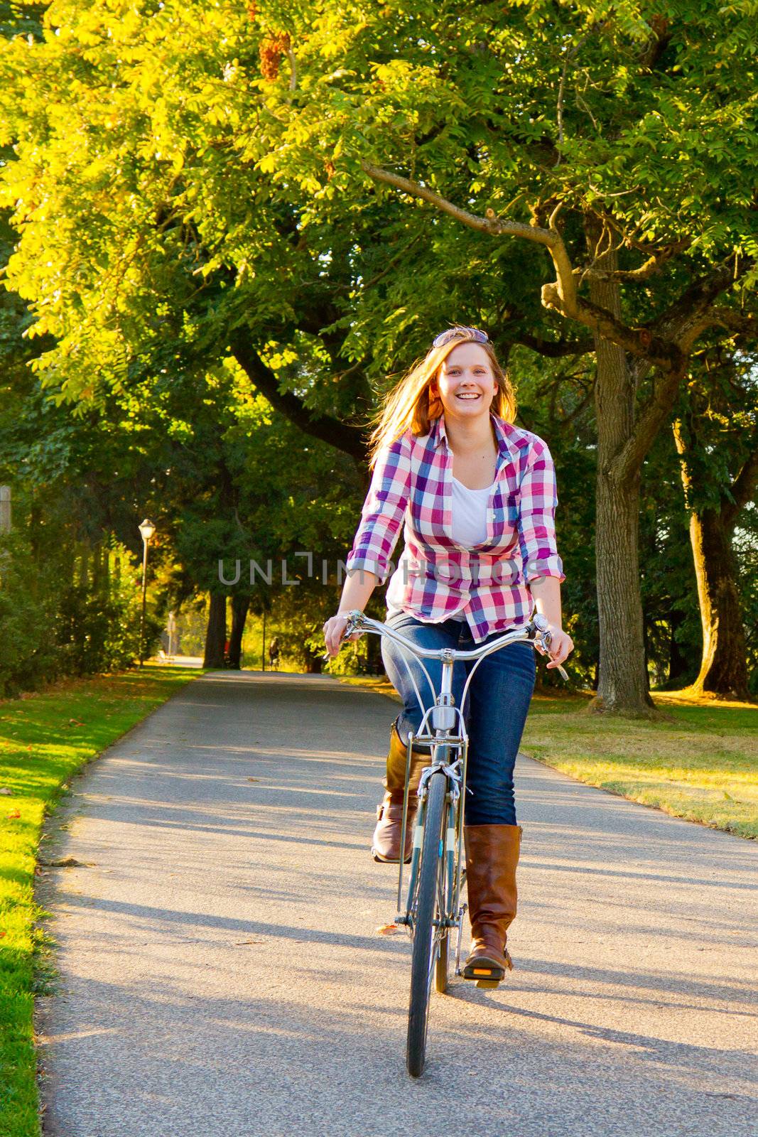 An attractive woman rides a bicycle along a path through a park.