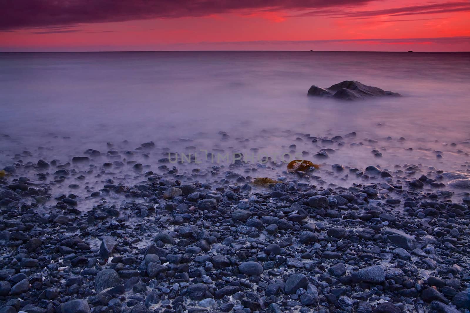 Pebble beach with red skies by sunset on Lofoten islands in Norway