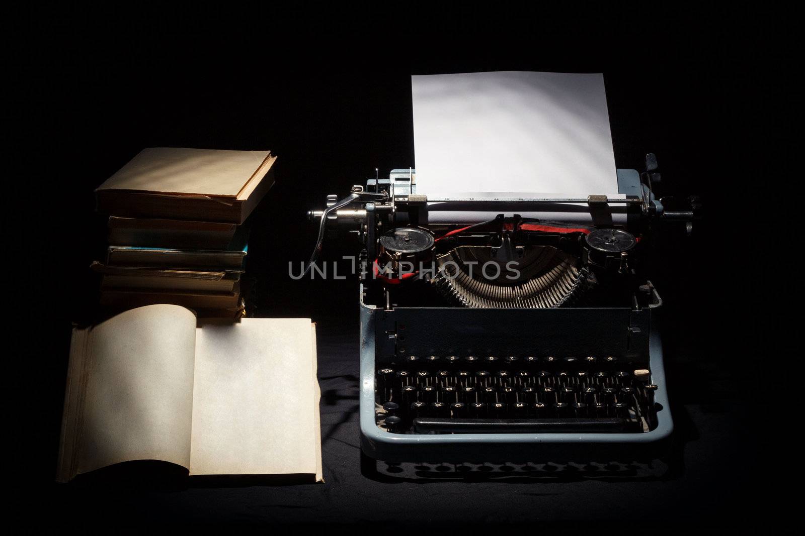 retro typewriter with stack of book and one opened book black background