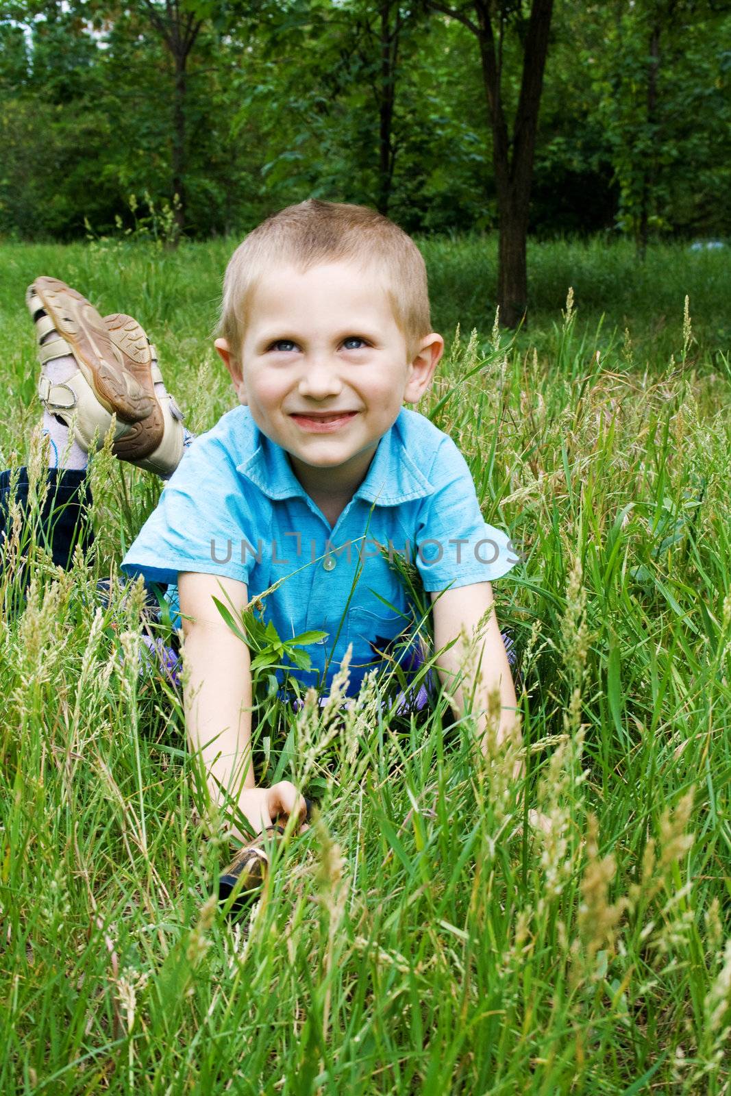 Little boy playing outdoors, lying on green grass