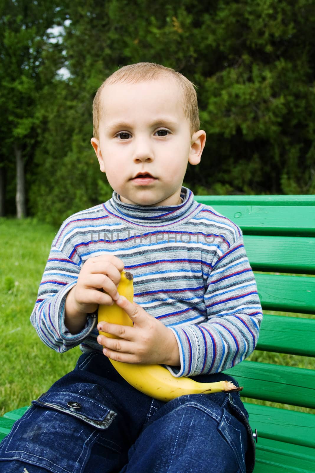 Boy outdoors sitting on a bench and cleans the banana