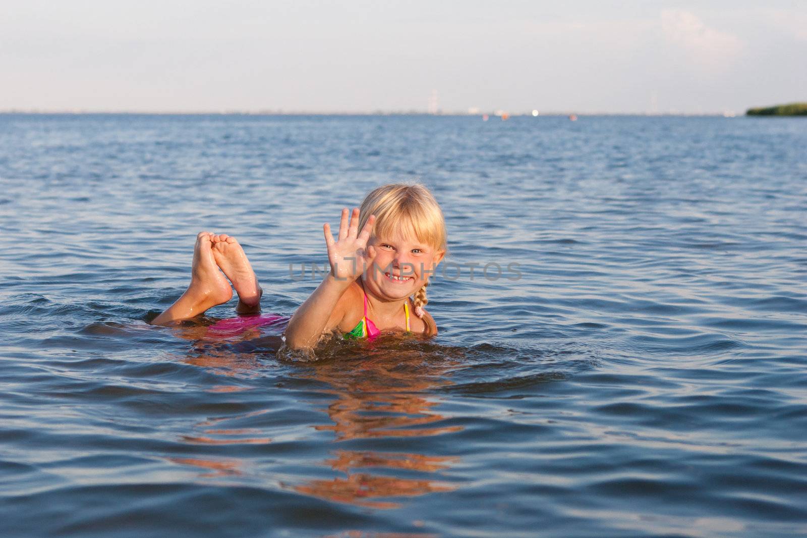 happy girl waving with hands in the water at the evening