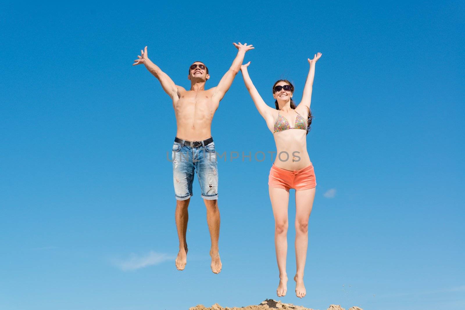 young couple jumping together on a blue sky background