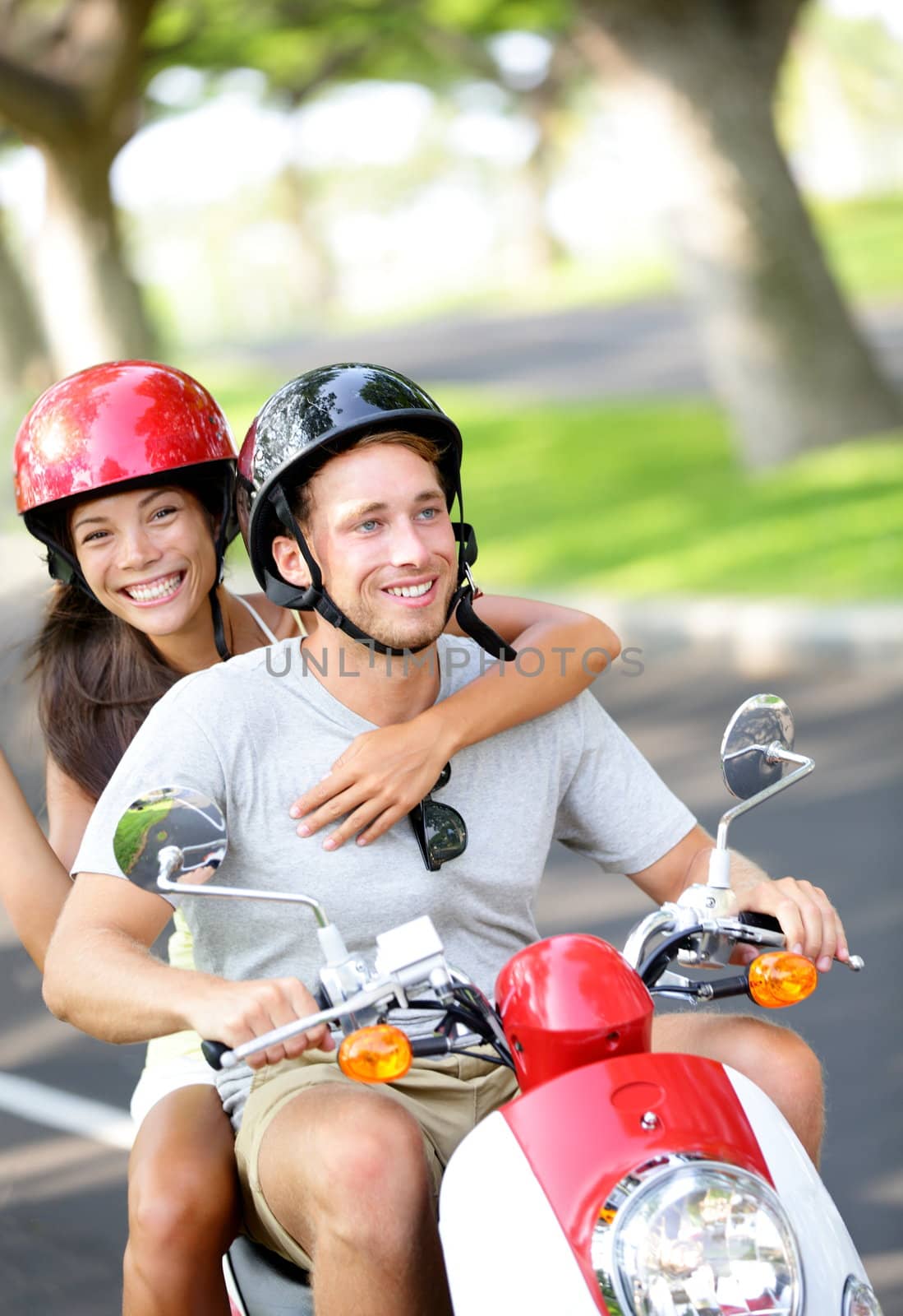 Free young couple on scooter on summer vacation holidays. Multiethnic happy couple having fun driving scooter together outdoor wearing helmets. Caucasian man, Asian woman.