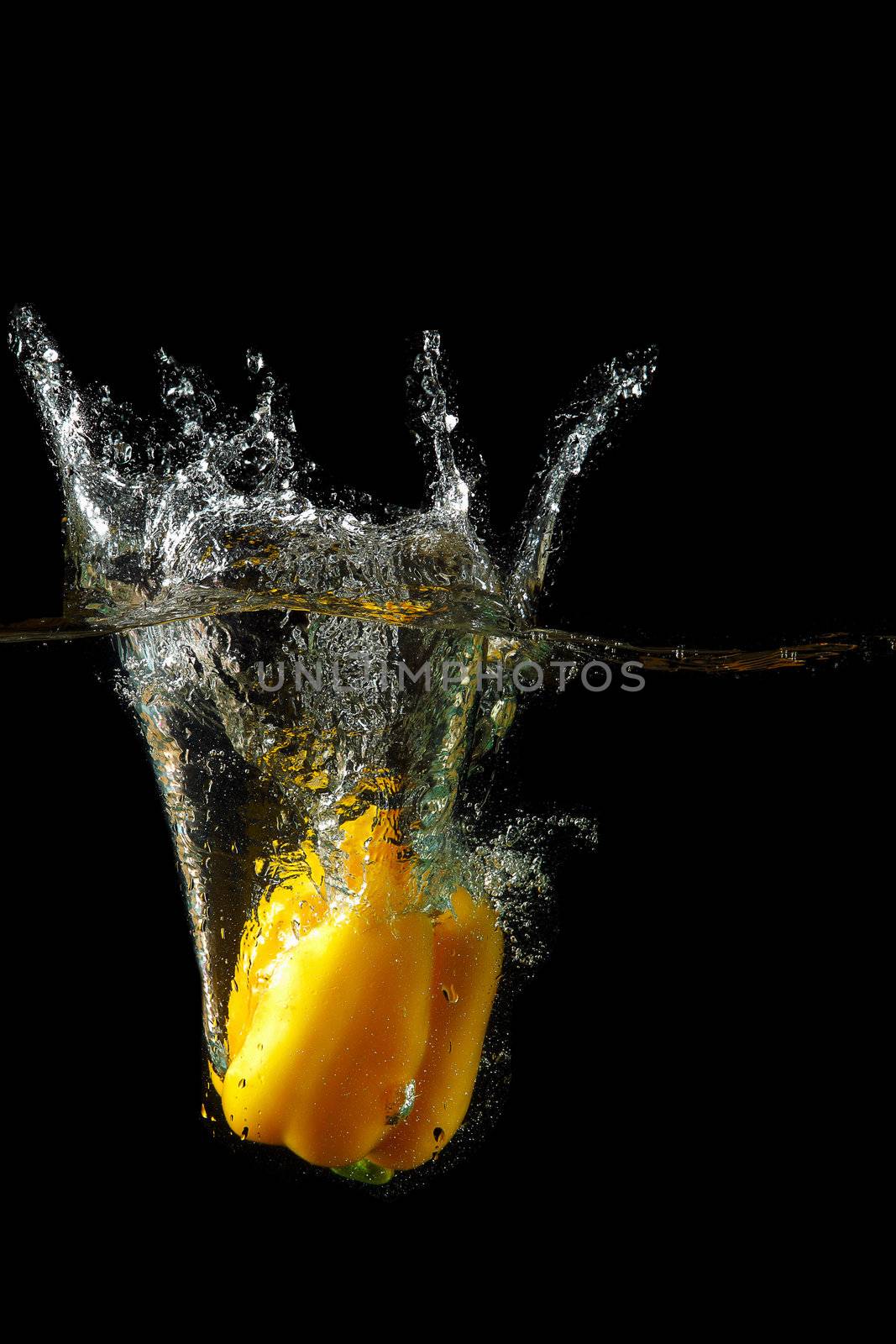 Colored yellow paprika in water splashes on black background