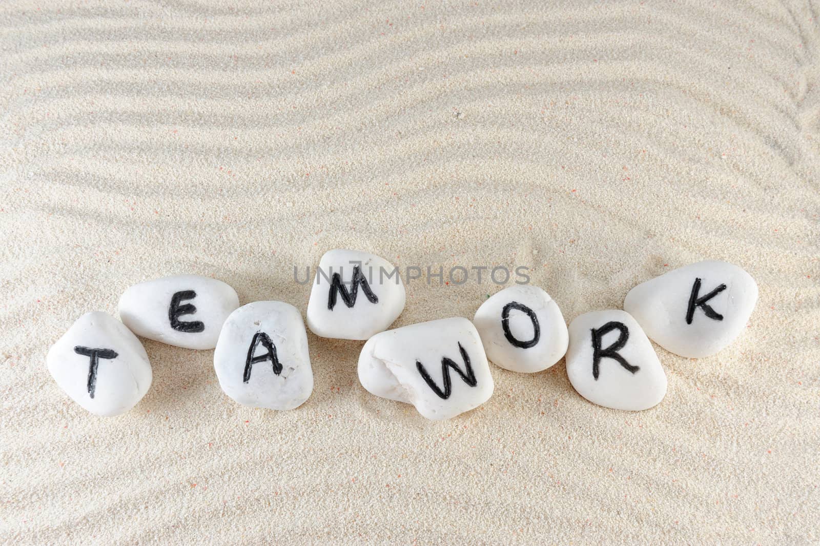 Teamwork word on group of stones with sand background