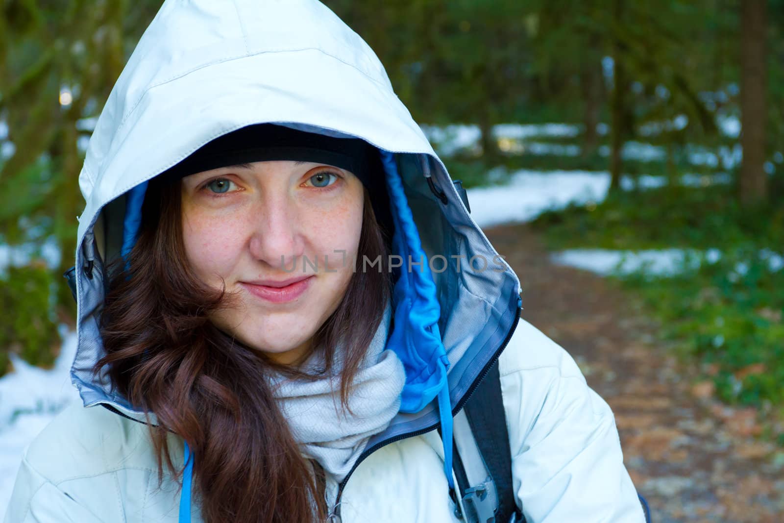 A woman pauses during her hike for a rest and to look at the camera while wearing a white jacket.