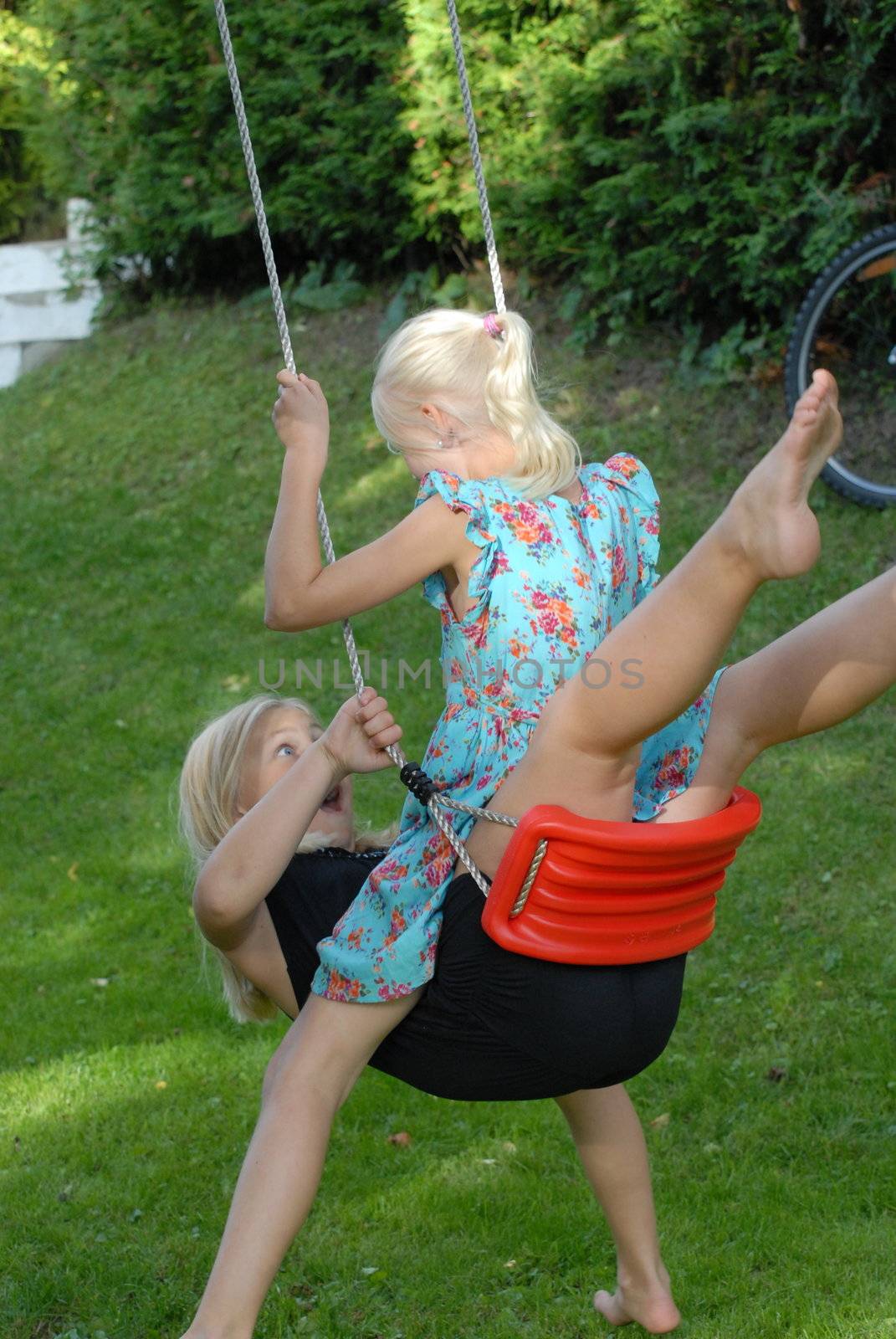 Girls playing on swing in garden. Please note: No negative use allowed