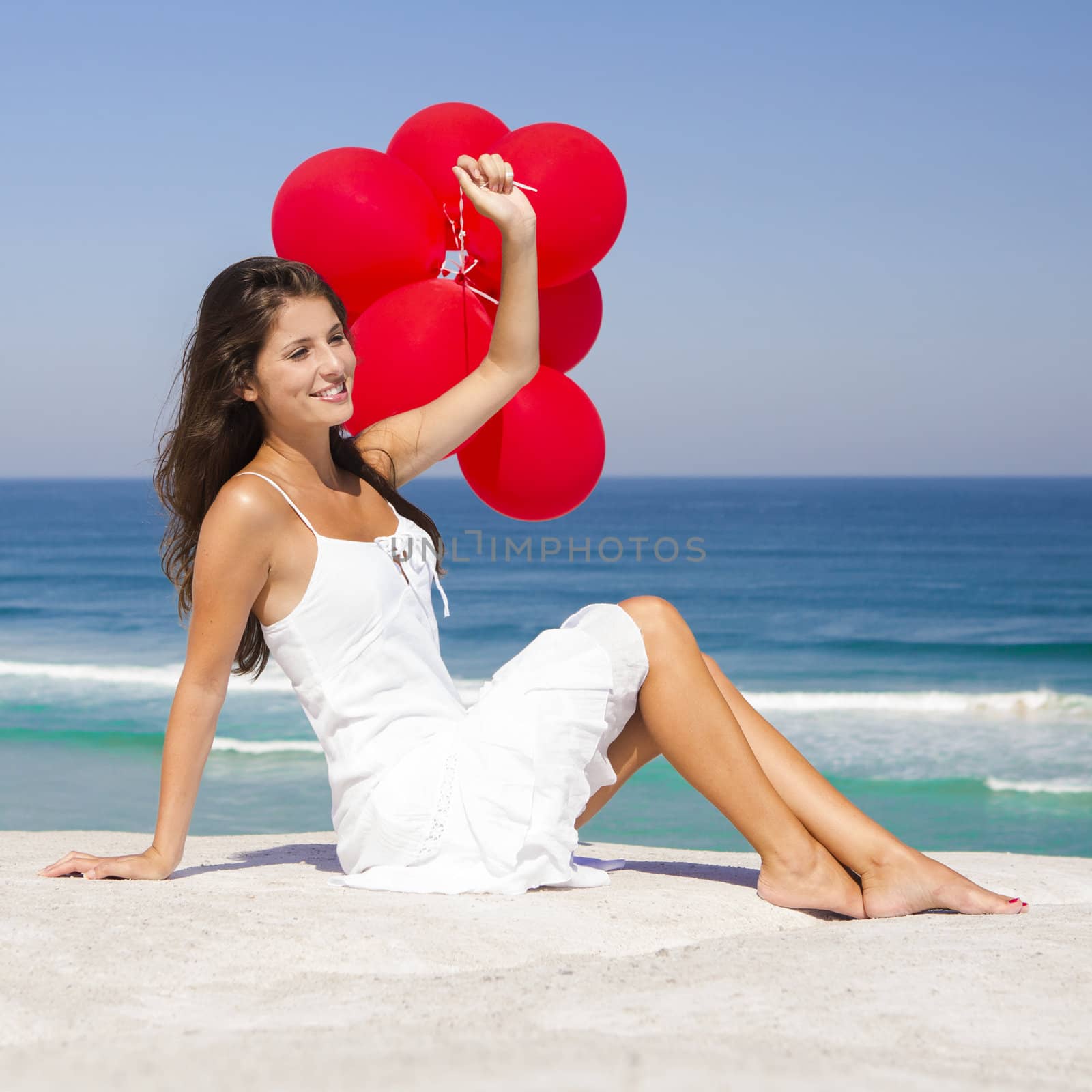Beautiful girl with red ballons sitting in the beach 