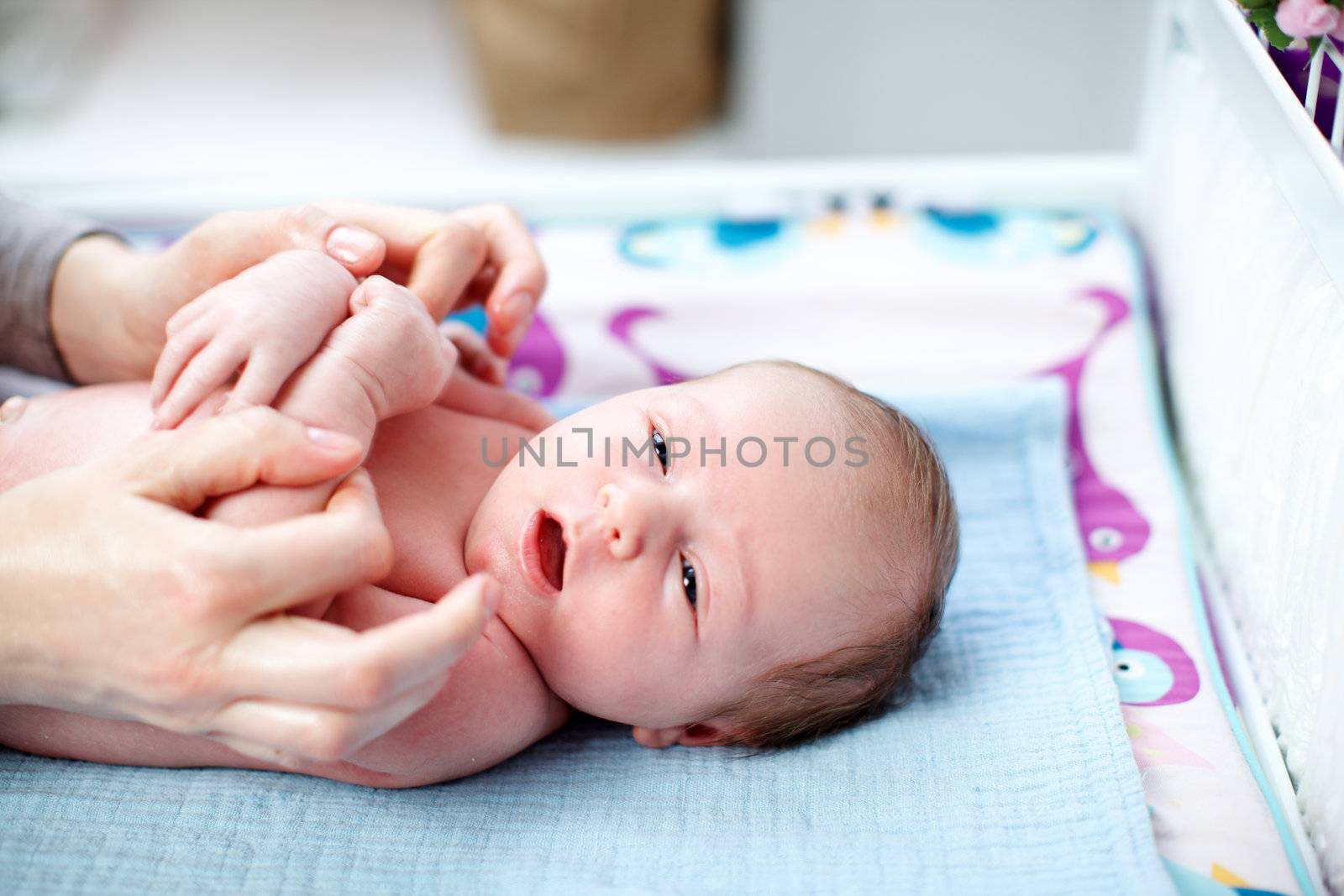 Cute sleepy newborn baby gazing at the camera as it lies on its back in the nursery cradled by the hands of the mother
