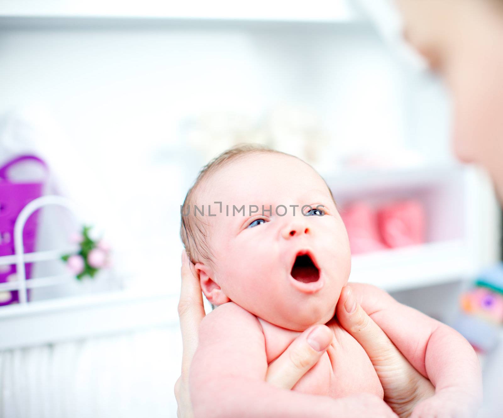 Cute yawning tiny baby being held in its mothers hands as she prepares to dress it in the nursery, closeup of the infants face