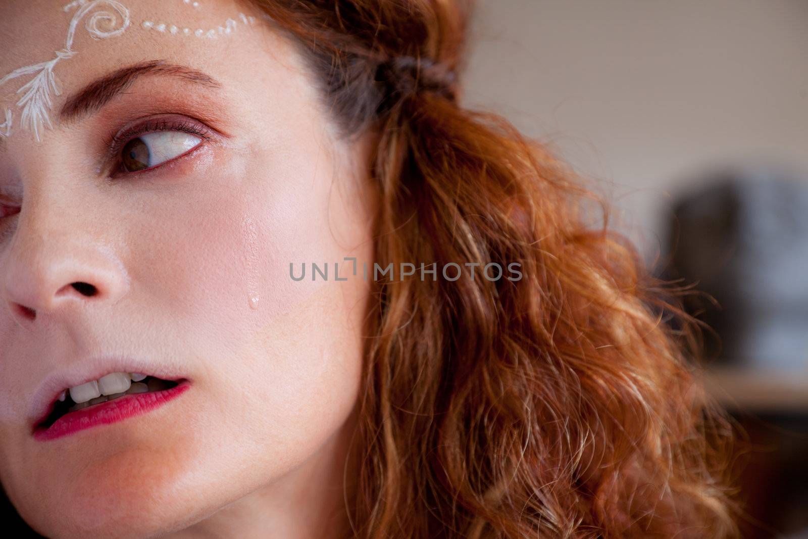 Portait of young sad woman crying with white henna tattoo on forehead, looking aside
