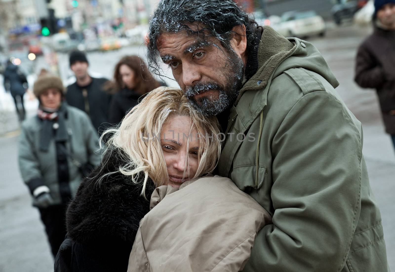 Struggling homeless frozen couple embracing in city centre