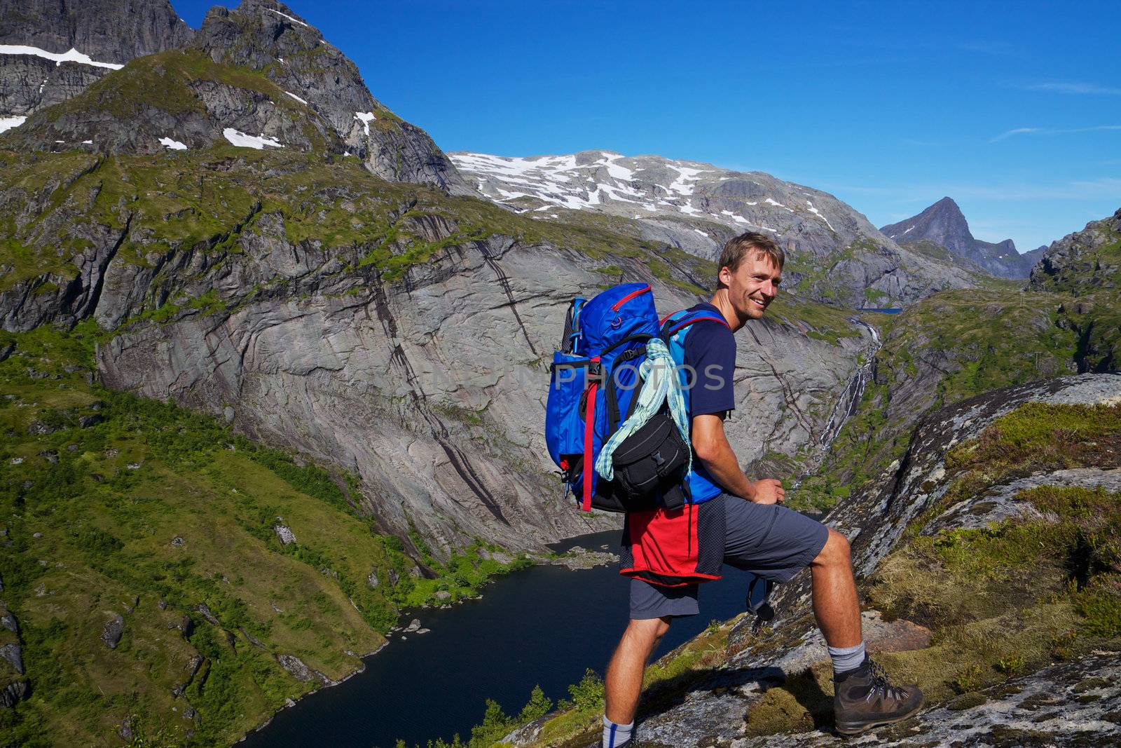 Young active man with backpack hiking on scenic Lofoten islands in Norway on sunny day