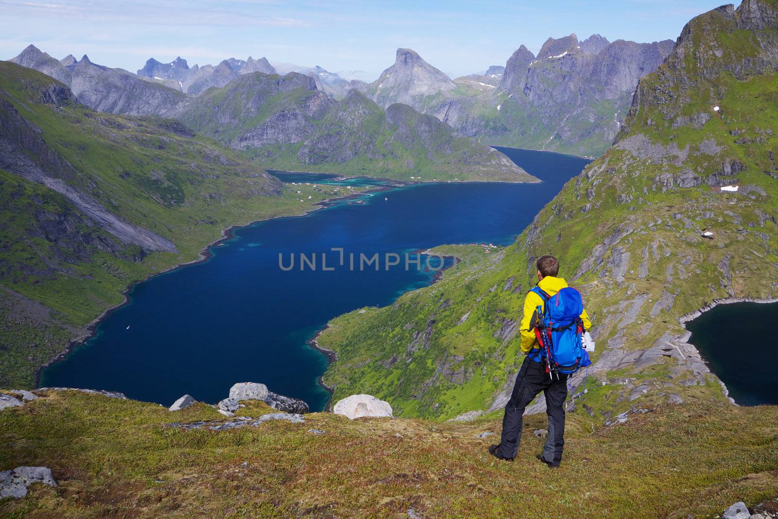 Young active man with backpack hiking on Lofoten islands in Norway on sunny day with scenic panorama in the background
