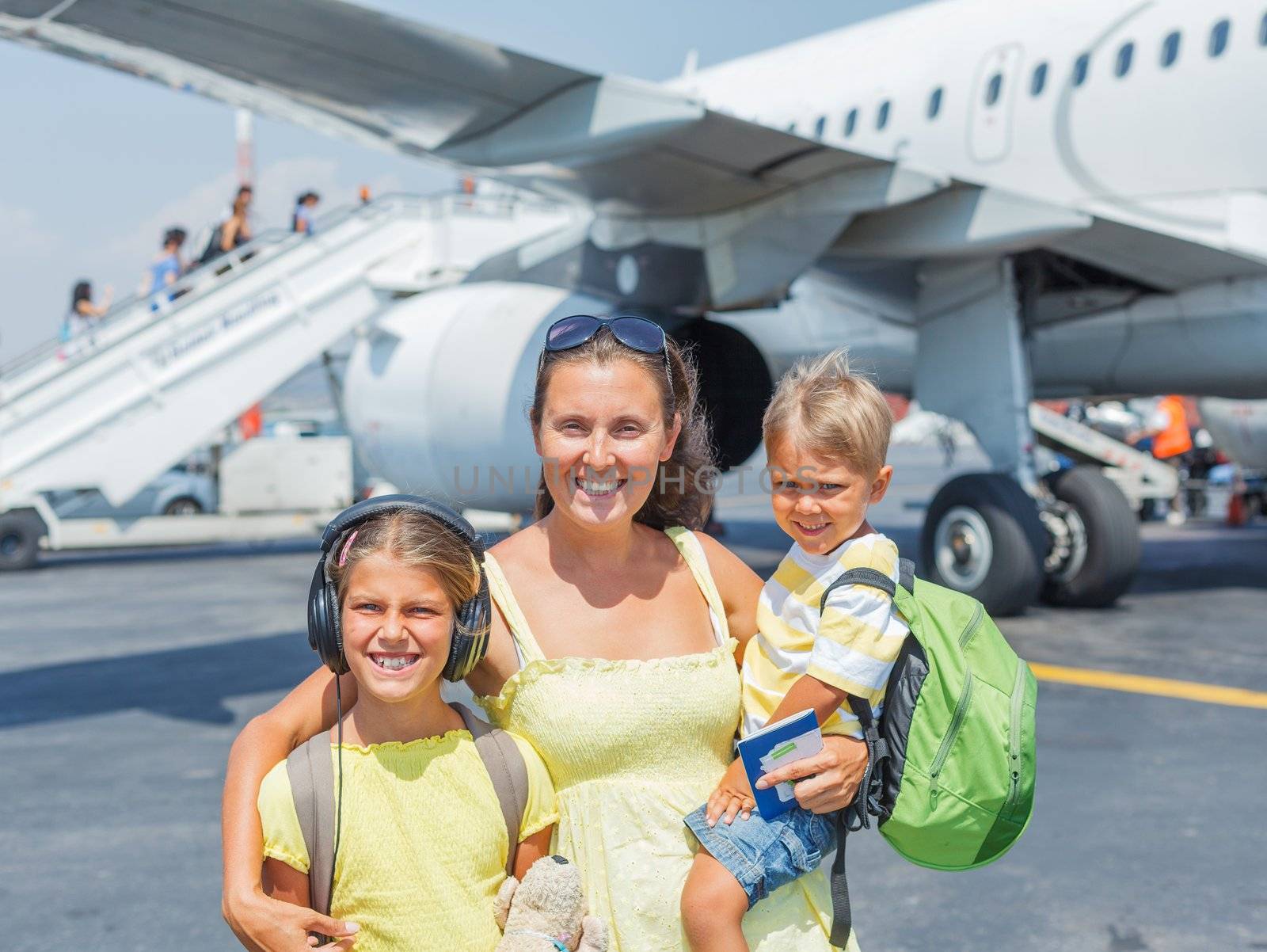 Young mother with two kids in front of airplane by maxoliki