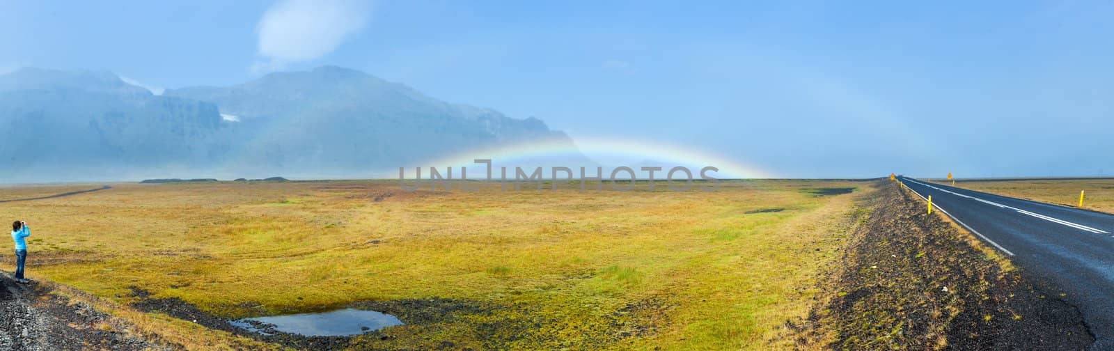 Rainbow over asphalt highway. Panorama. Iceland - famous Ring Road (Hringvegur).