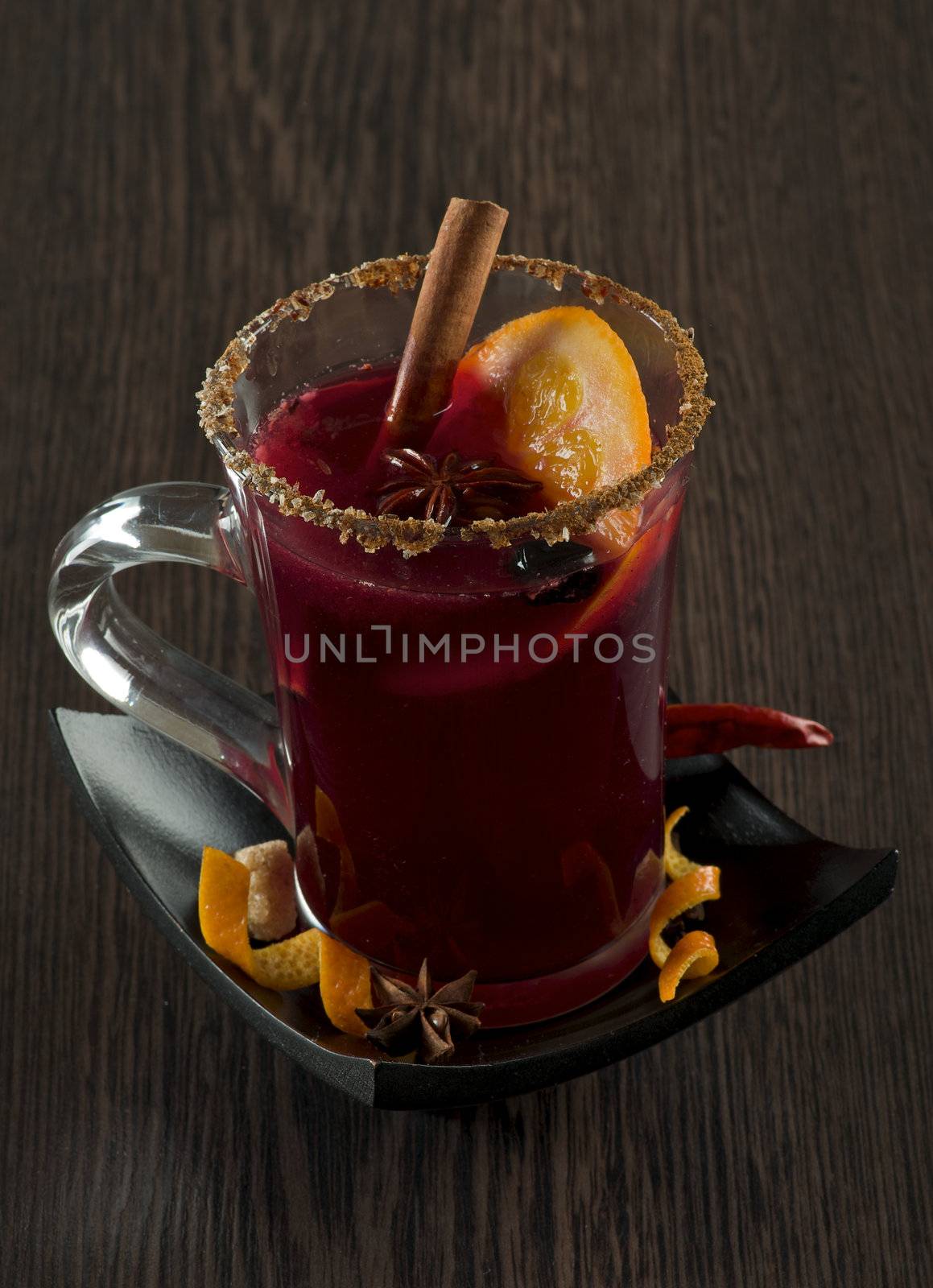 Glass of Mulled Wine and Spices with Cinnamon Stick, Orange, Anise Star and Sugar on Black Saucer closeup Wood background