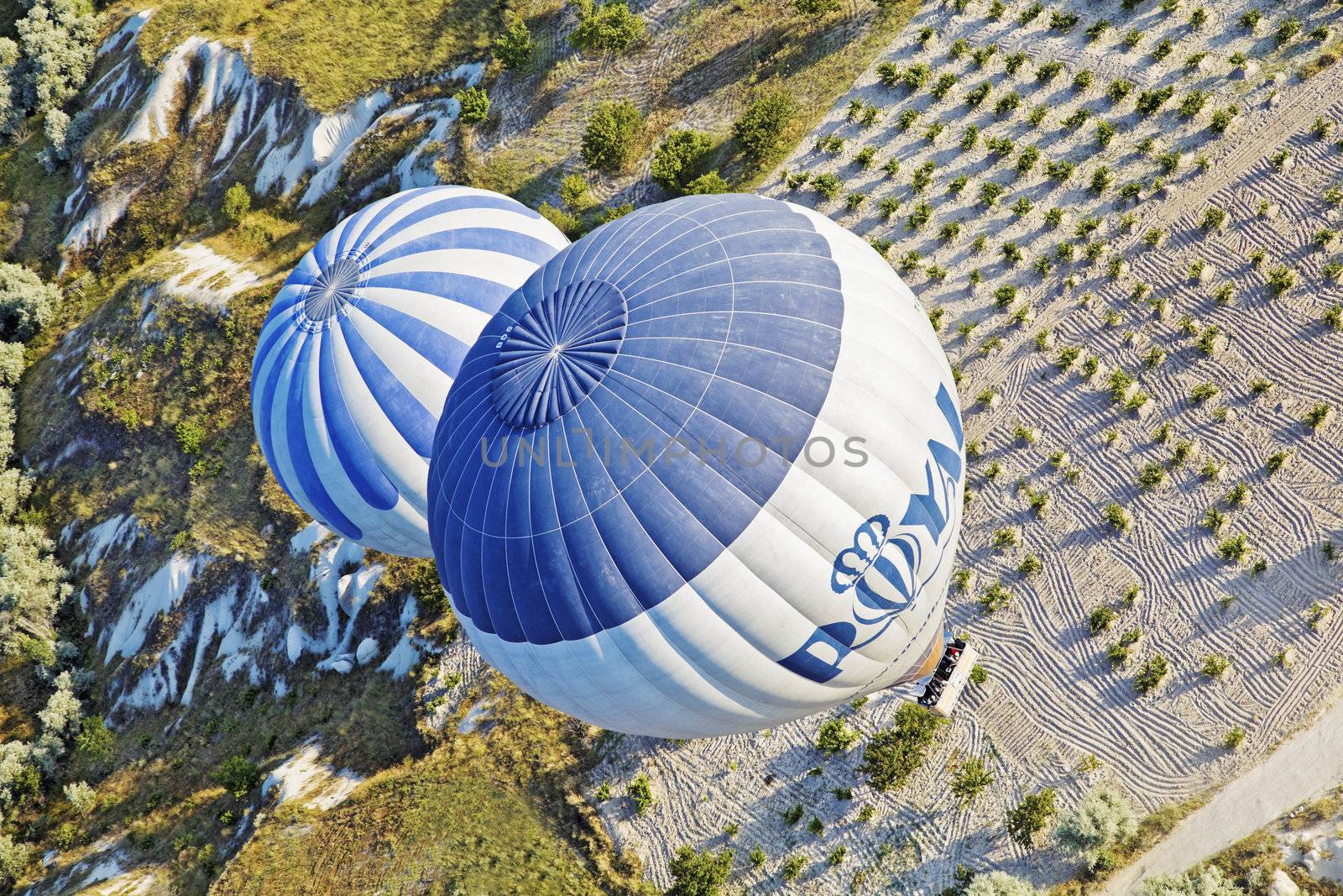Diagonal aerial shot of two hot air balloons on a low level flight path over the interesting limestone agricultural land of Cappadocia, Turkey