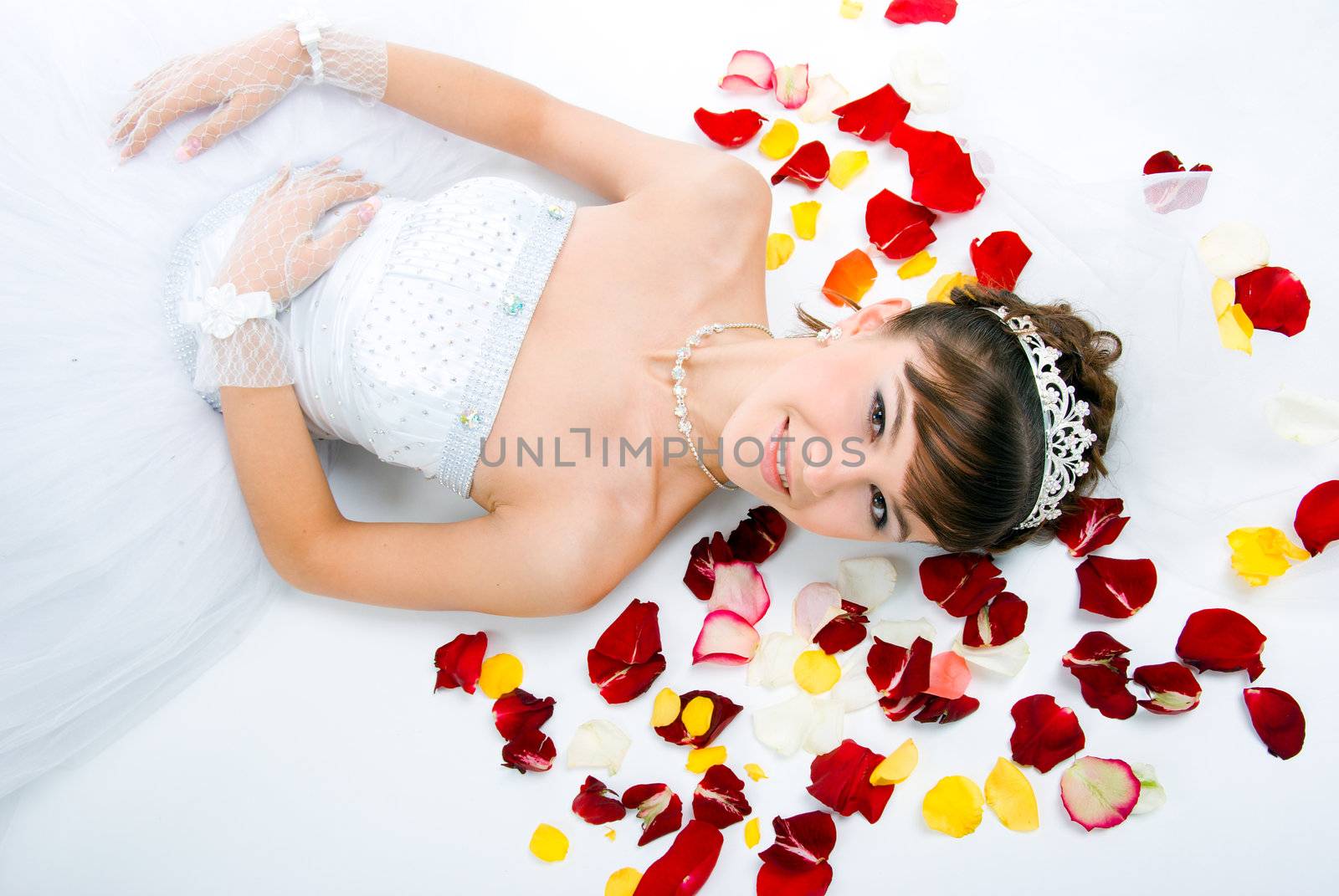 Beautiful sexy bride on  floor among red rose petals on white background 