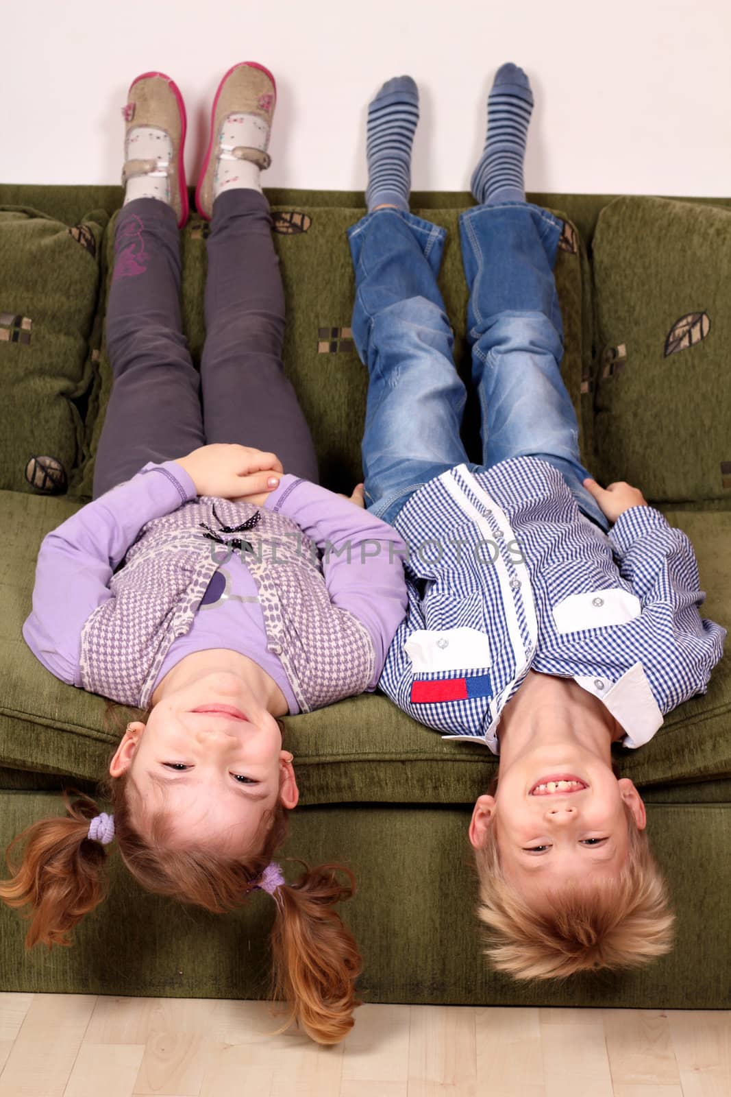 little girl and boy lying upside down on the bed by goce