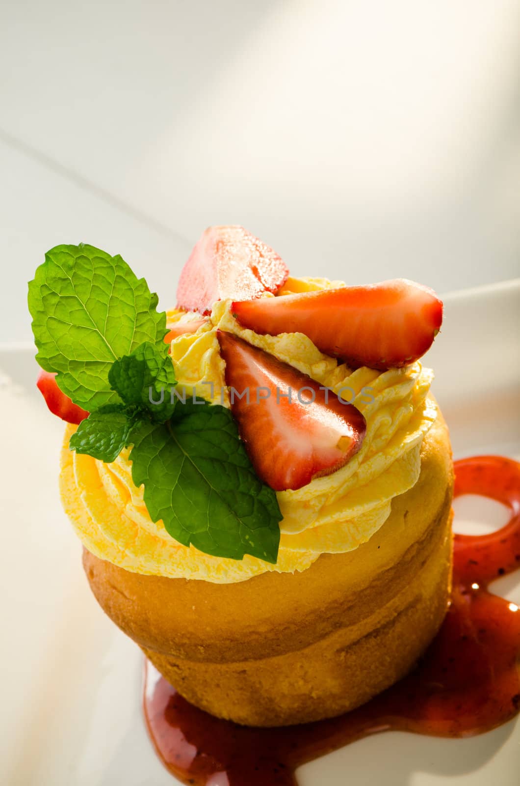 cupcake with yellow cream fresh mint leaves and strawberry as decoration strawberry sauce on the plate