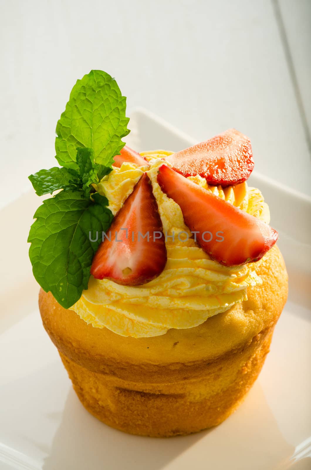 cupcake with yellow cream fresh mint leaves and strawberry as decoration on white plate