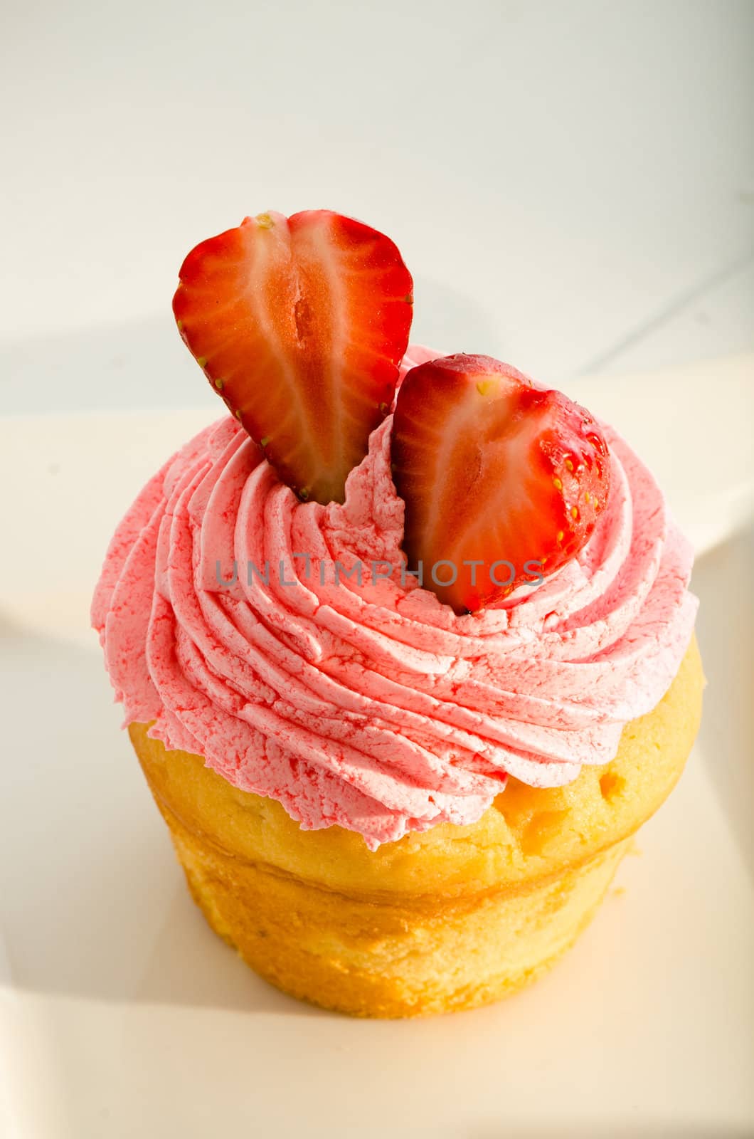 strawberry cupcake and two fresh strawberry on the top. White plate and fork