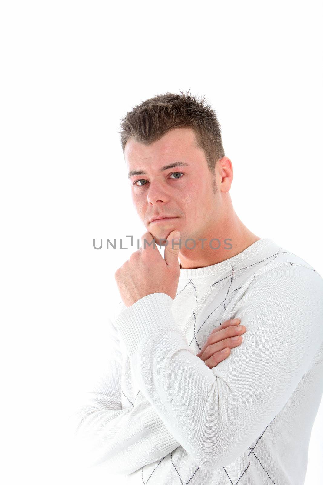 Serious young man deep in thought standing sieways with his hand to his chin looking at the camera isolated on white