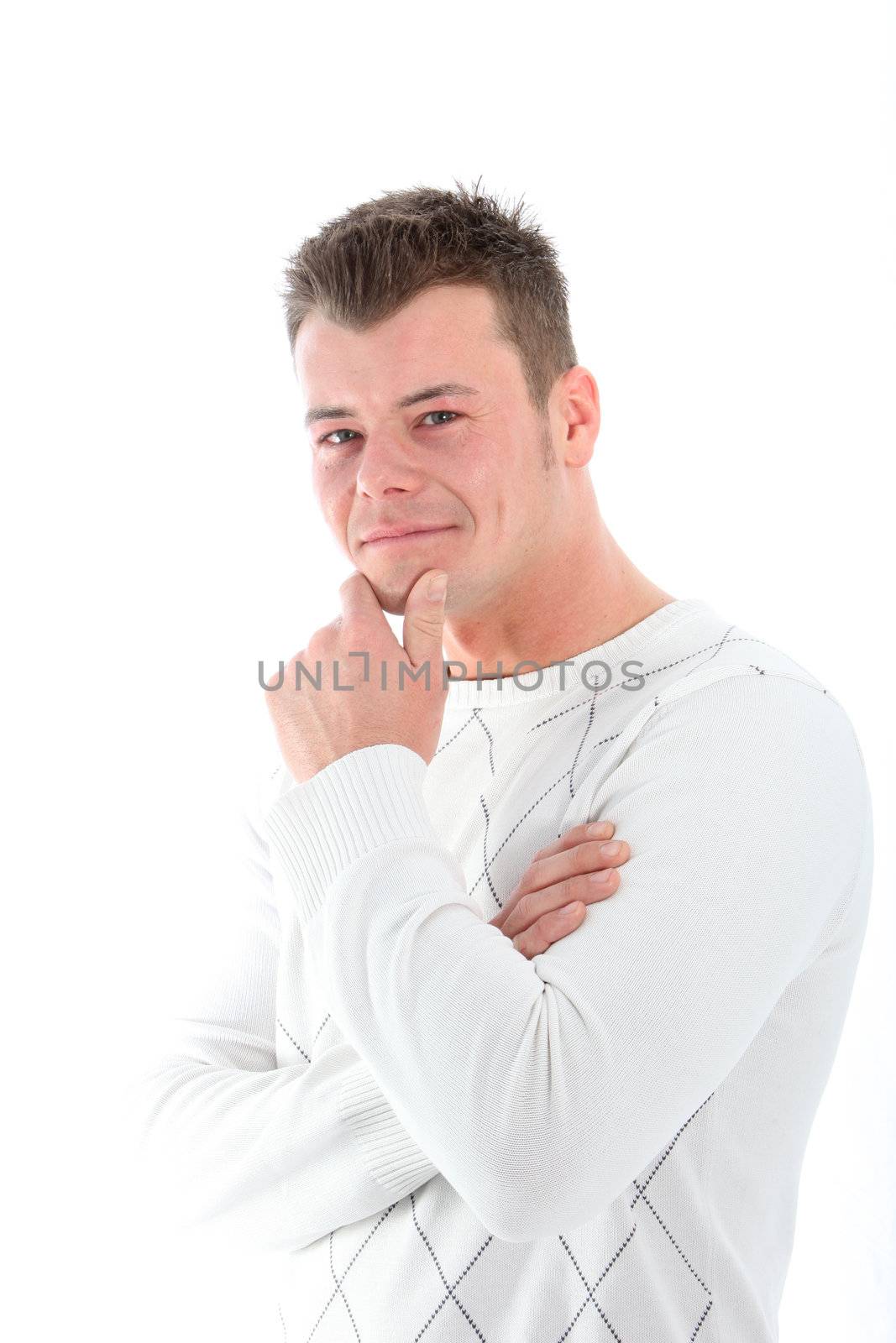 Thoughtful handsome young man with an amused smile standing at an angle looking at the camera with his hand to his chin isolated on white