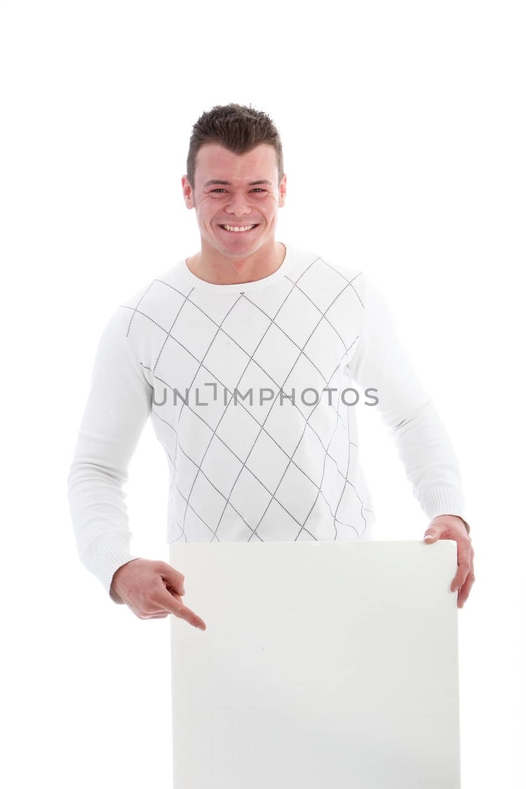 Beaming handsome young man pointing to a blank white sign which he is holding below his waist, isolated on white