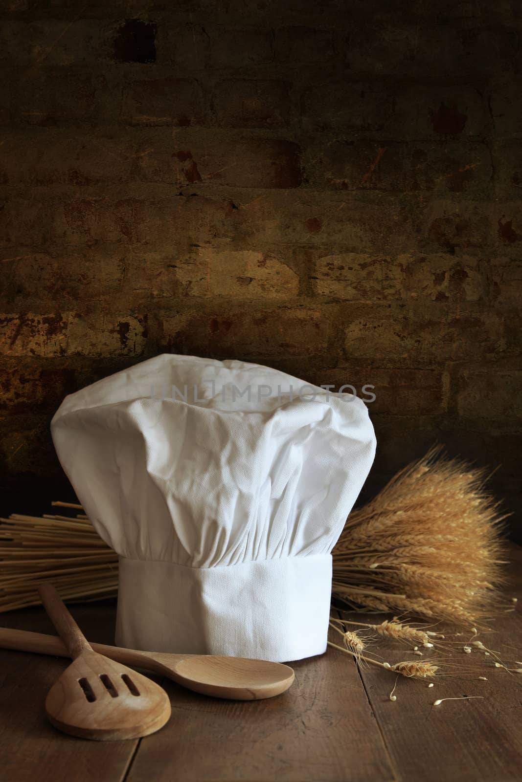 Chef hat and wooden spoons and wheat with brick background