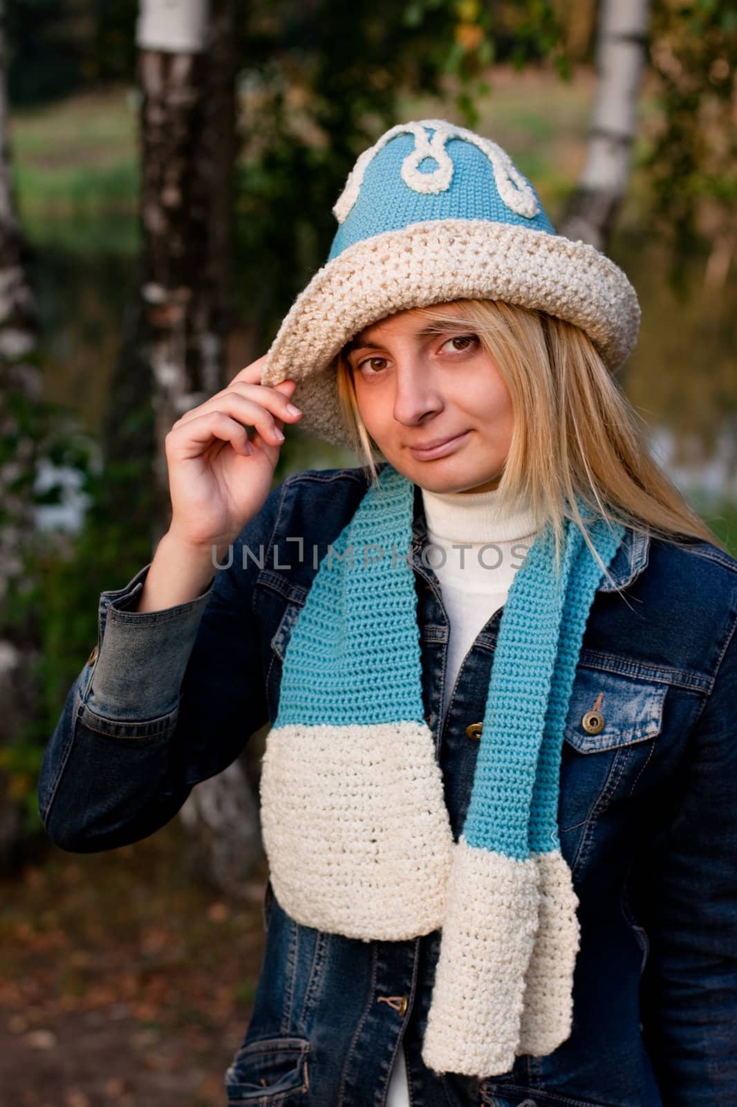 A blonde girl in a beret and scarf and jeans coat in a forest
