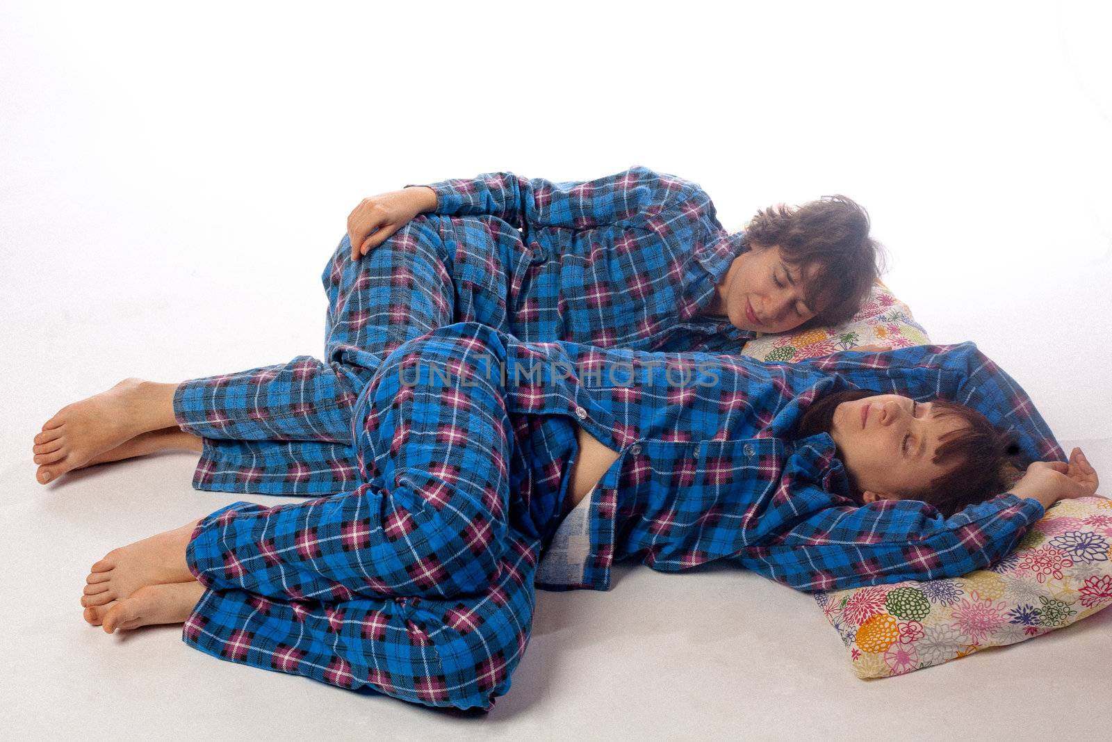 Two girls sleeping on big pillows on white
