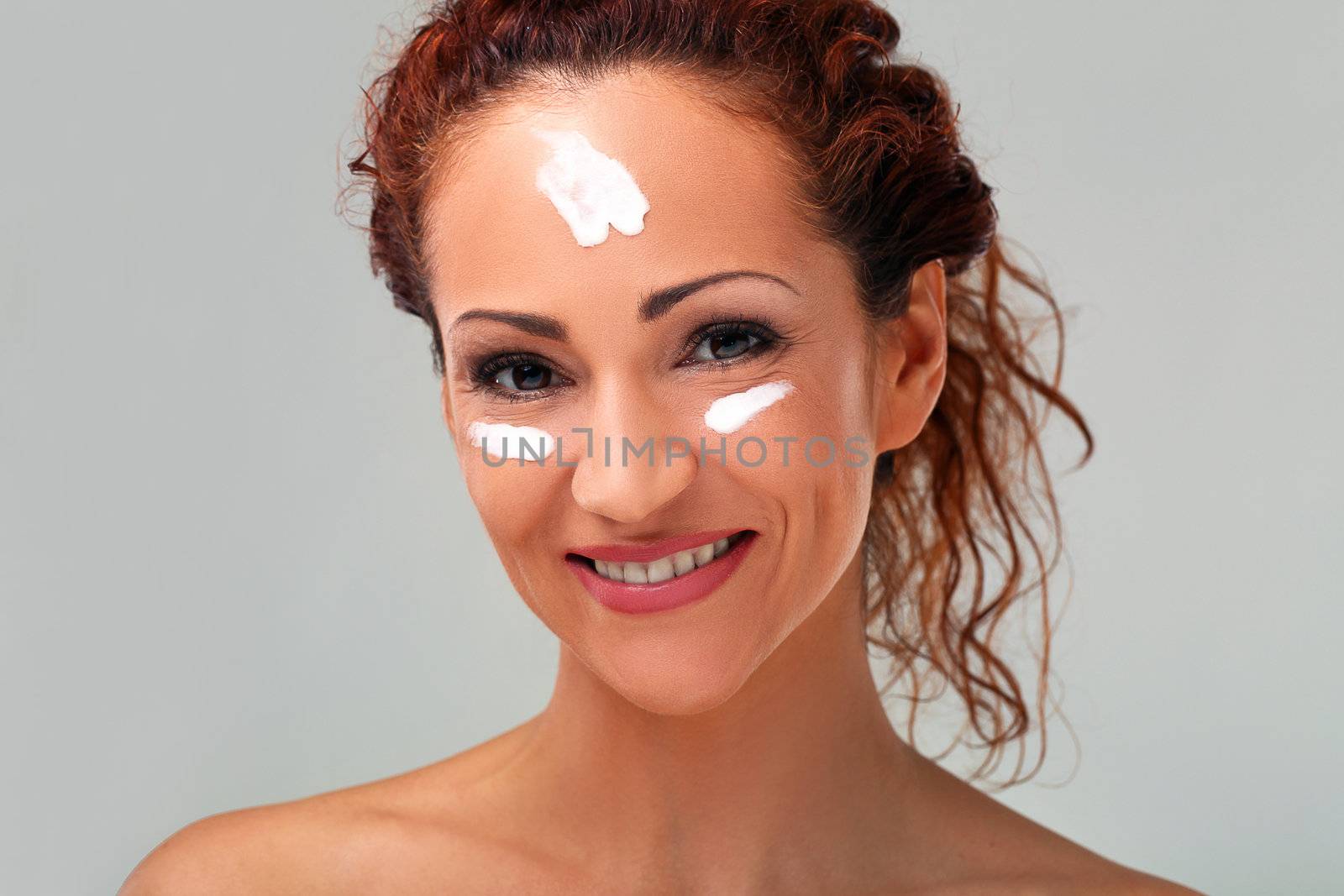 Beautiful natural middle aged woman cover face with cream isolated on grey background