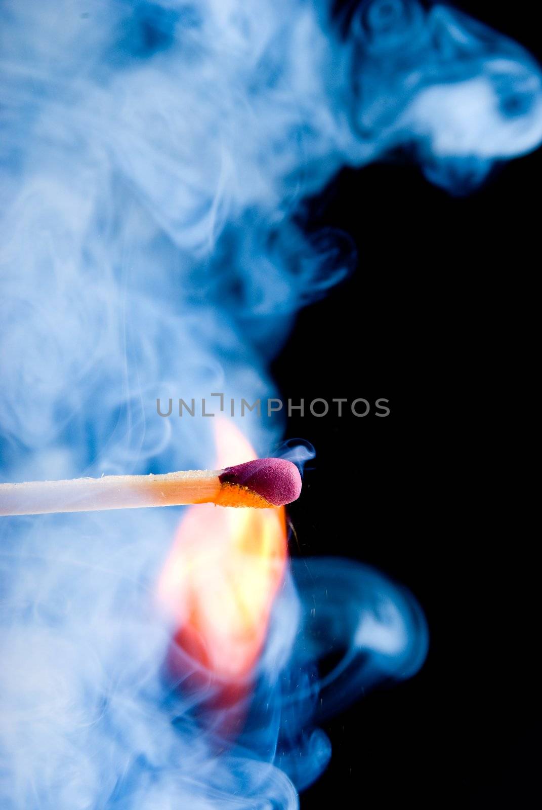 Burning match with blue smoke over black background