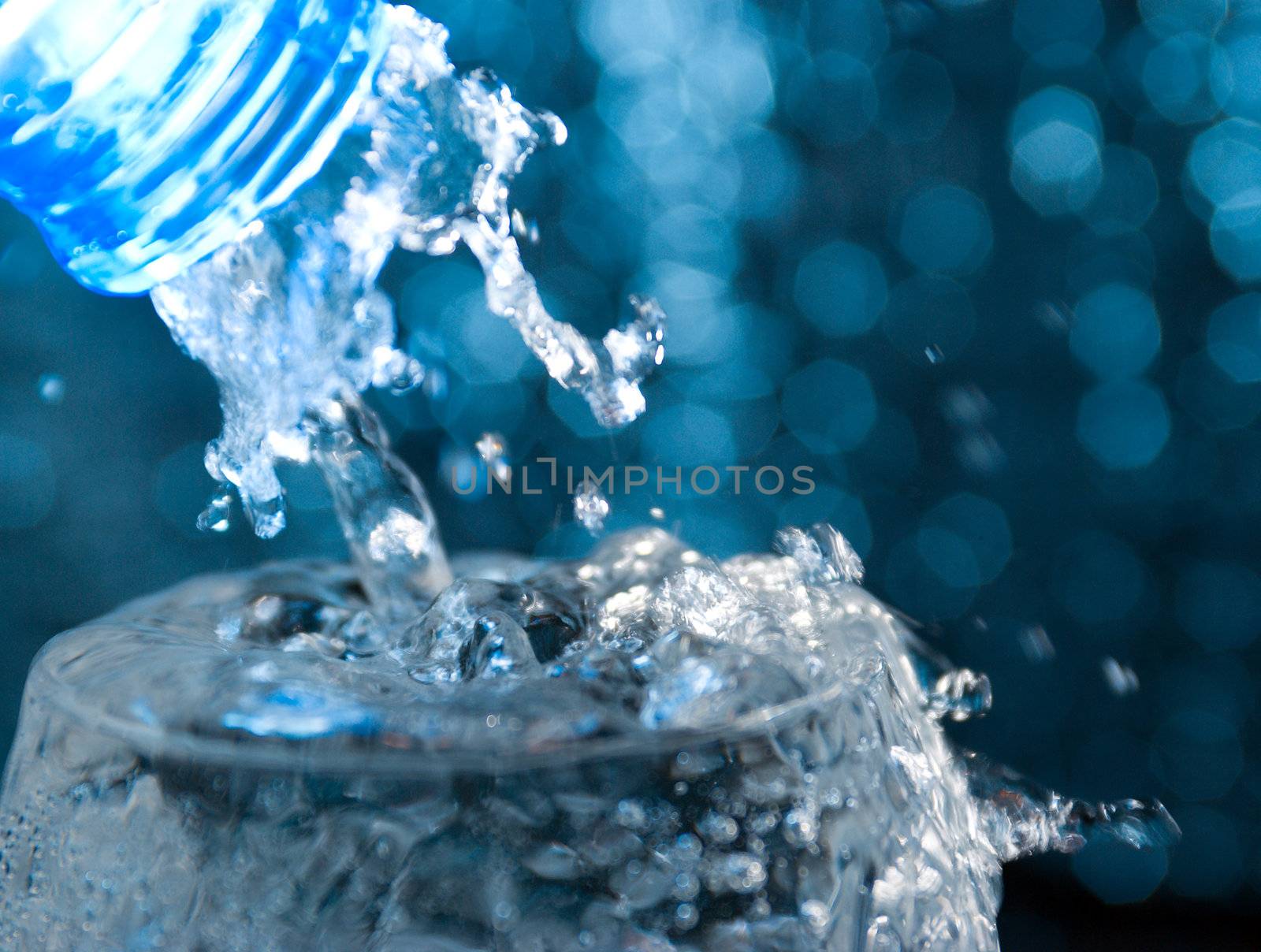 Bottle with creative splashing water.Macro of water poured into a glass of water 