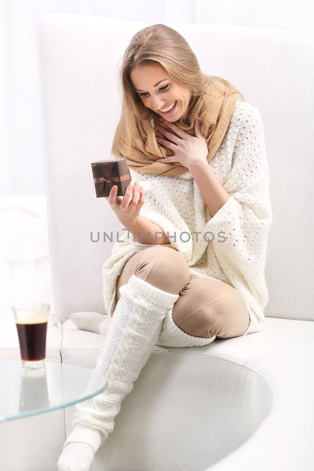 Long-haired young blonde woman sitting on a sofa. He holds a box with a present. She is surprised and very happy.







Young long-haired blonde sitting on a sofa with a present