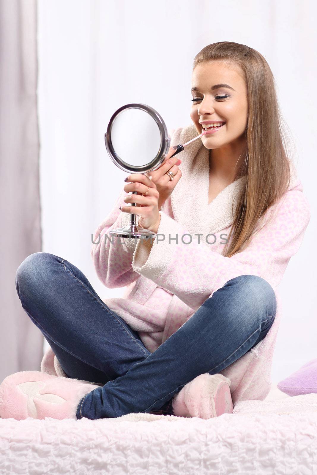 Young long-haired blonde girl in a bathrobe sitting on the bed, lips gloss paints