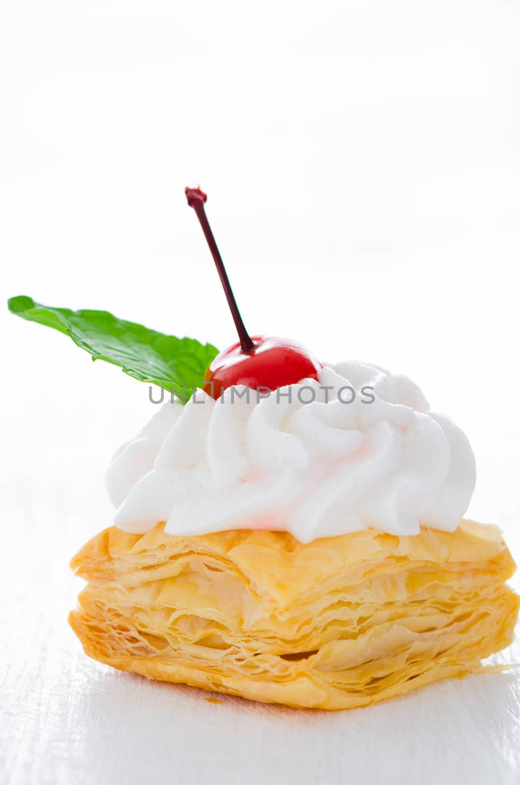 puff pastry cake with cream cherry and fresh mint leaf on white plate