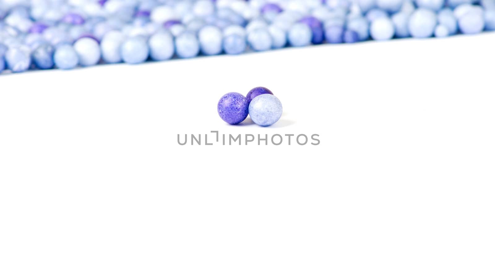 One blue and two violet little pearls isolated on background of other pearls.