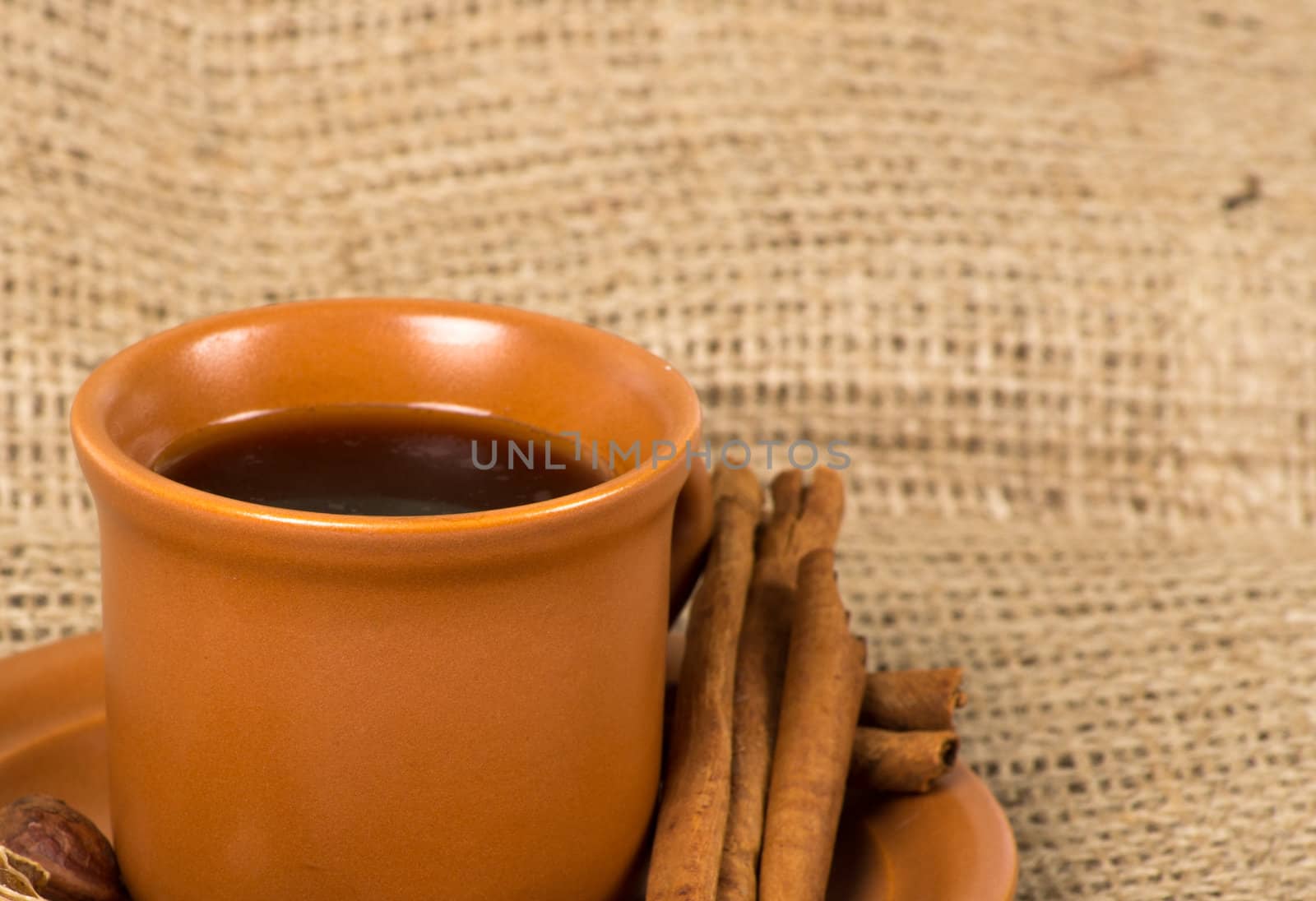 Coffee cup with cinnamon, coffe beans, nuts and lemon over sacking