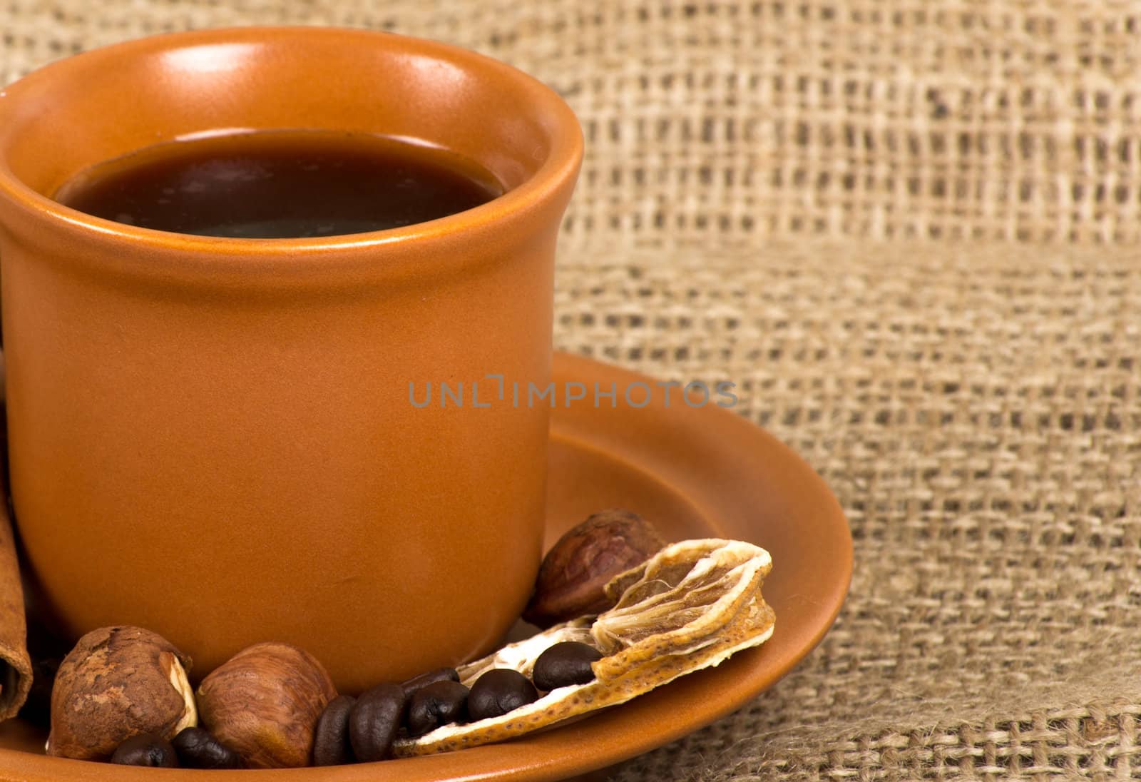 Coffee cup with cinnamon, coffe beans, nuts and lemon over sacking