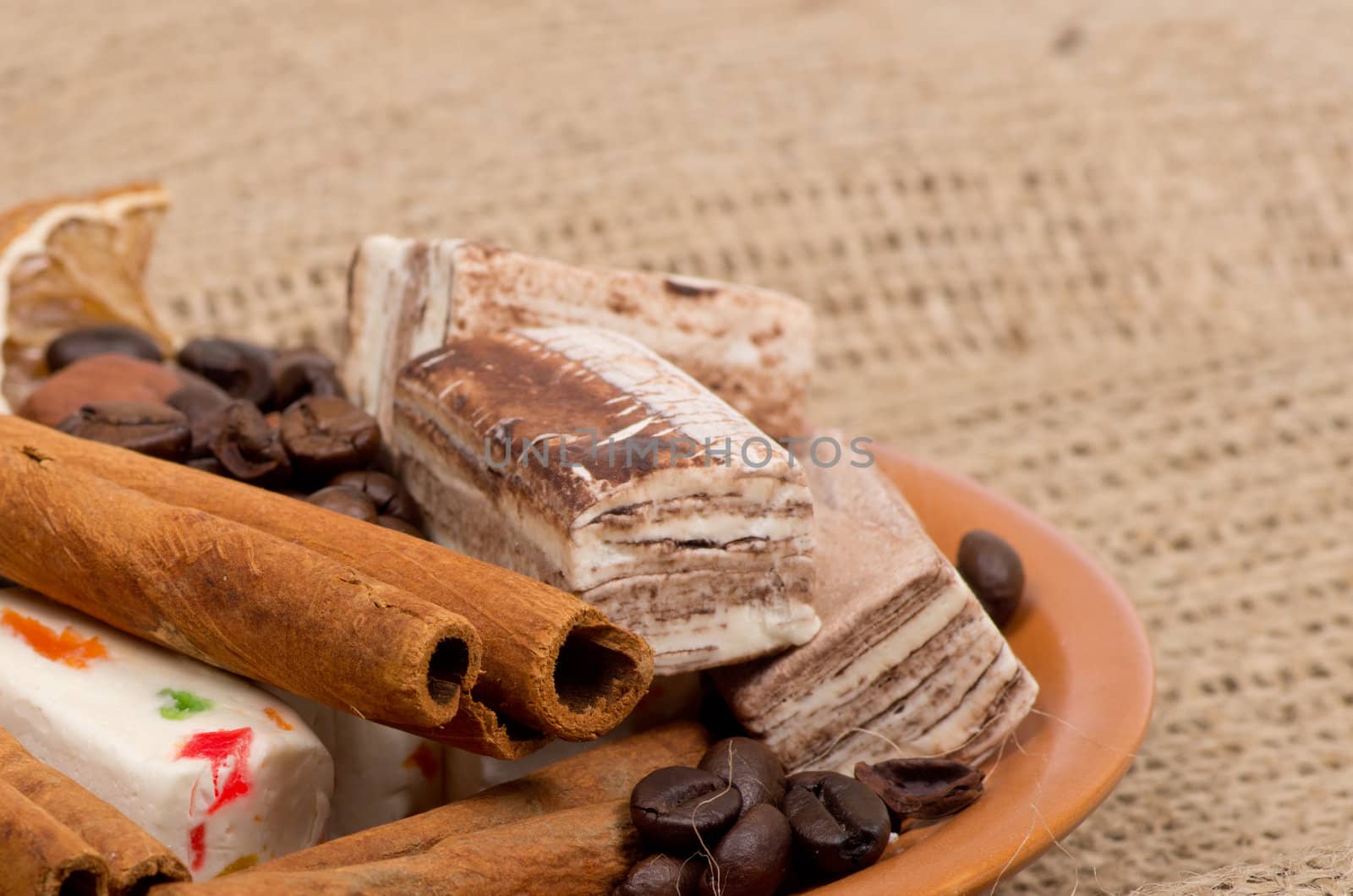 Sweets, cinnamon, nuts and coffee beans on a saucer, on burlap background.